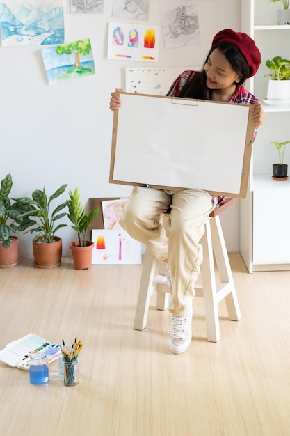 Young girl sitting on a chair with easel for drawing hold Color palette and brush in the room