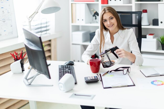 A young girl sitting at a computer Desk in the office and pours his coffee.