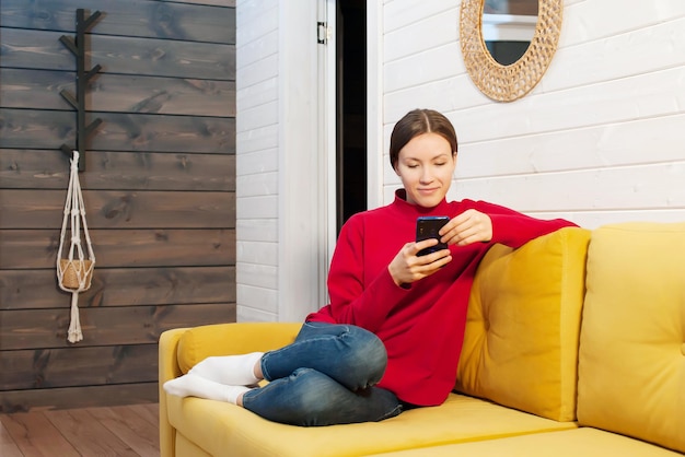 young girl sitting on the couch at home and using a mobile phone Communicates on social networks
