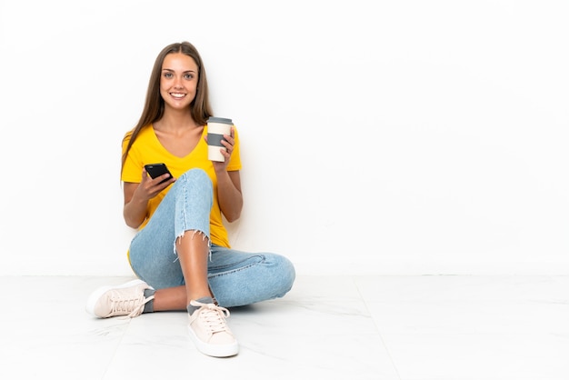 Young girl sitting on the floor holding coffee to take away and a mobile