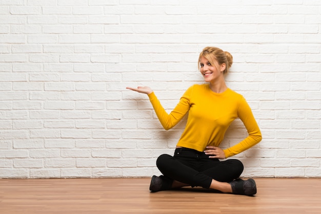 Young girl sitting on the floor holding copyspace imaginary on the palm to insert an ad