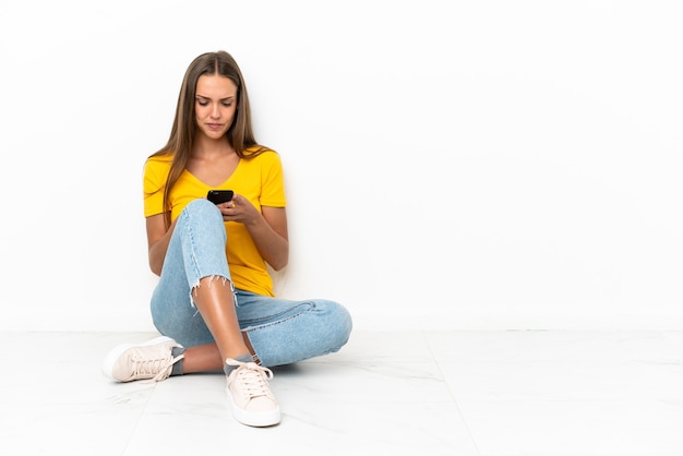 Молодая девушка сидит на полу, отправляя сообщение с мобильного телефона