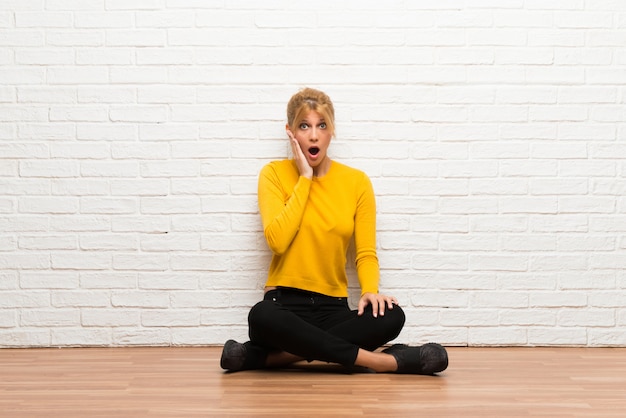 Young girl sitting on the floor surprised and shocked while looking right