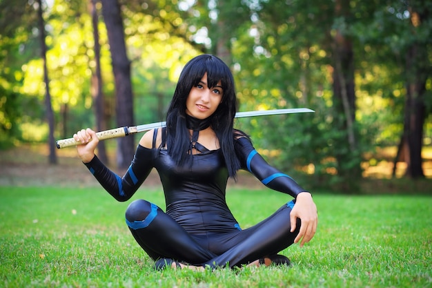 Young girl sitting on the grass and holding samurai sword. Original cosplay character
