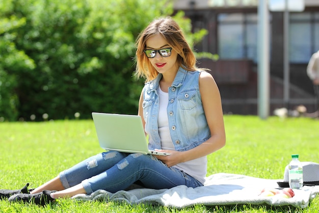 Young girl sitting on the grass with laptop