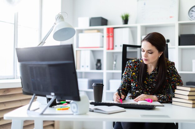 A young girl sitting in the office at the computer Desk and working with a book.