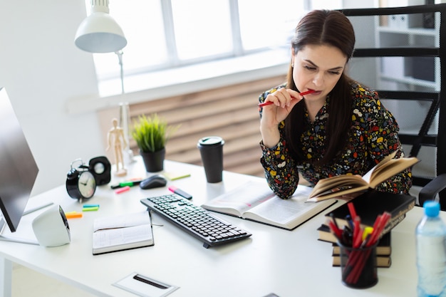 A young girl sitting in the office at the computer Desk and working with a book.