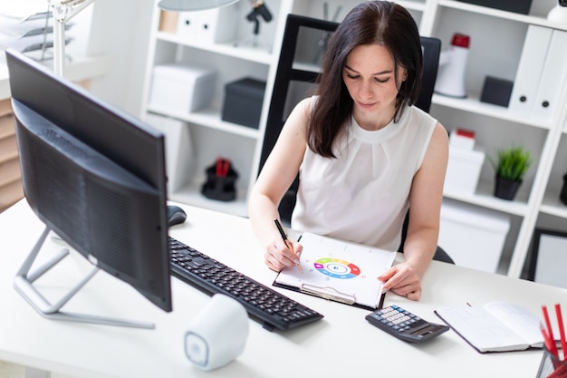 A young girl sitting in the office at a computer Desk and working with documents.