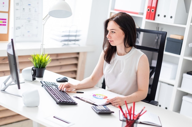 A young girl sitting in the office at a computer Desk and working with documents.