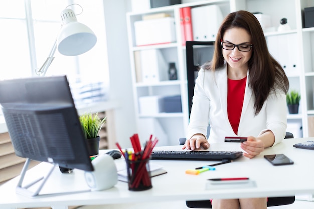 A young girl sitting in the office at the table and holding a Bank card.