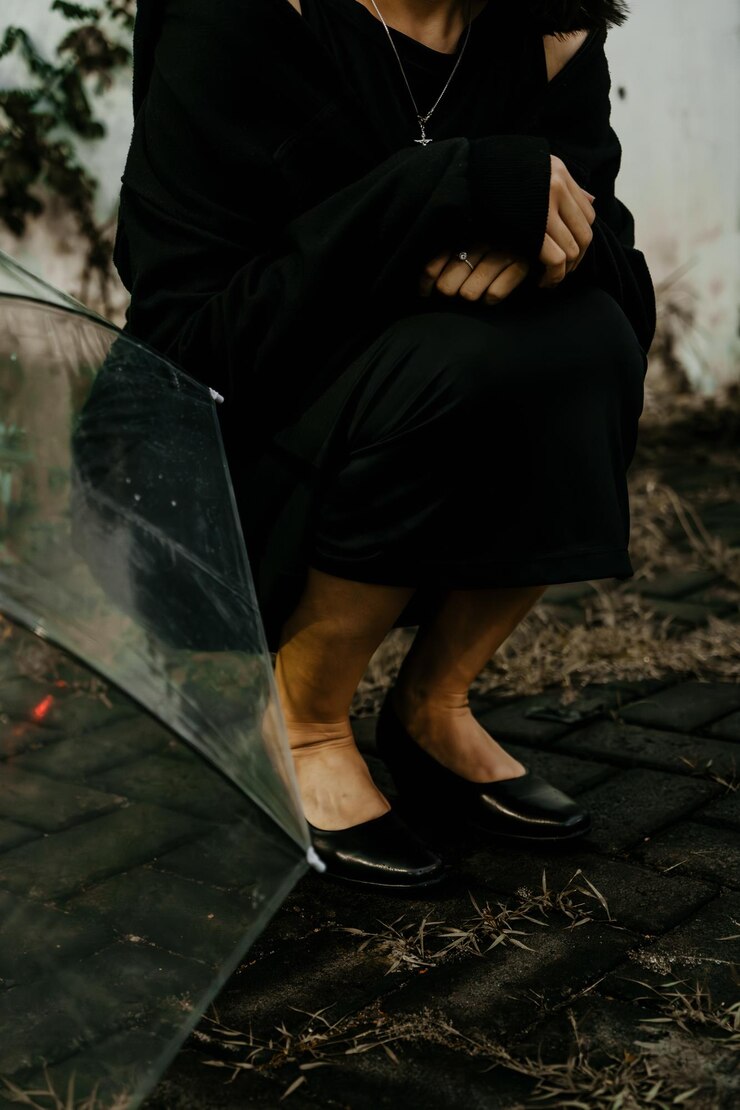 A young girl sitting under the rain with an umbrella on a black dress
