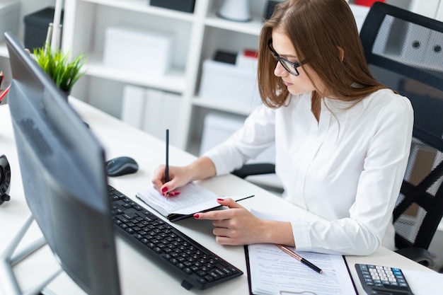 Ragazza che si siede al tavolo e che lavora con un computer, documenti e calcolatrice