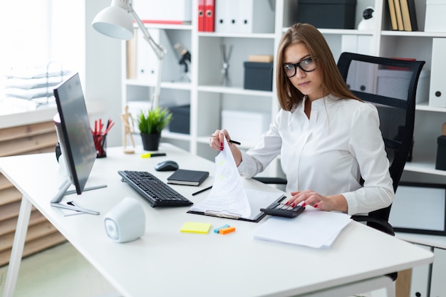 Young girl sitting at the table and working with a computer, documents and calculator