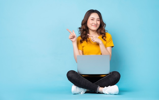 Young girl sitting using laptop with expressions and gestures on turquoise