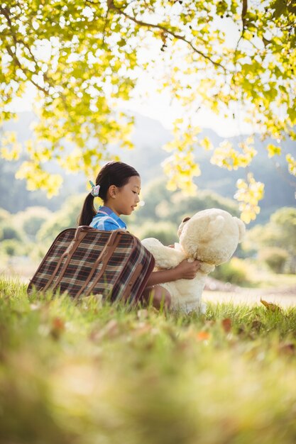 Young girl sitting with a teddy bear and suitcase