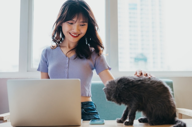 Young girl sitting working on sofa and cat sitting next to laptop