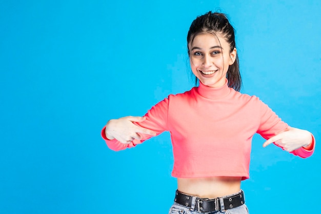 Young girl smiling and pointing fingers in front of herself on blue background