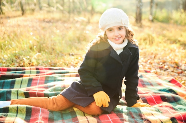 Young girl smiling while sitting on a blanket in the park in autumn. High quality photo