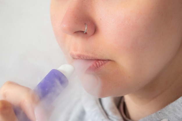 A young girl smokes a disposable ecigarette White background