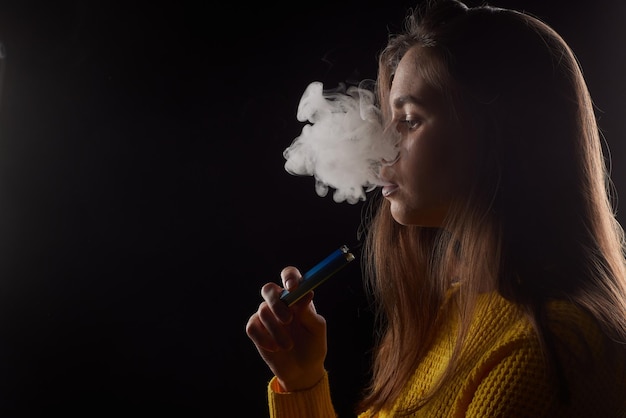 Young girl smokes a vape closeup on a dark background