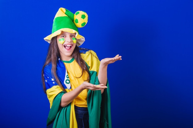 Young girl soccer fan from Brazil dressed in hat and flag presenting something