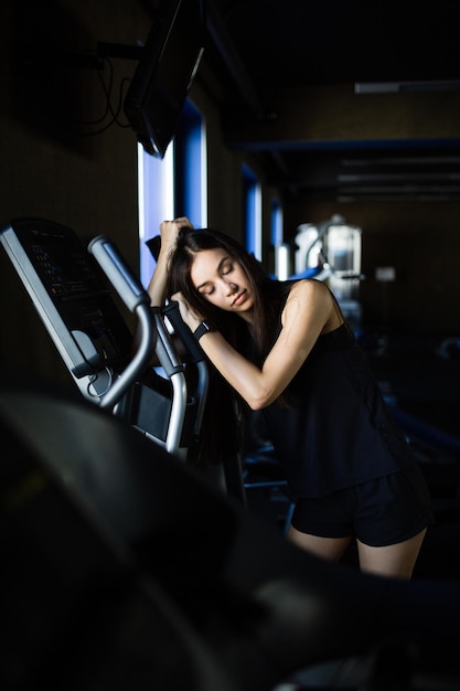 Young girl in sportswear tired near by modern sports simulator in gym club