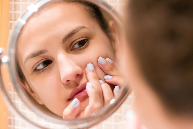 Young girl squeezes pimple on the fer face in front of a bathroom mirror Beauty skincare and wellness morning concept