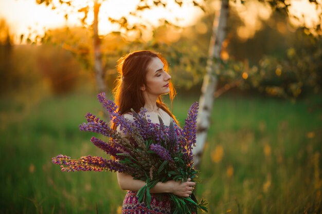 Basamento della ragazza nel campo che trascura il giacimento della lavanda. ragazza caucasica spensierata sorridente in vestito che gode del tramonto