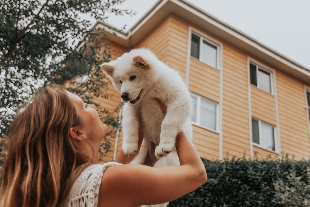 Молодая девушка, стоя назад, держа в руках щенка самоедской собаки снаружи. Имея концепцию домашнего животного. Концепция милые животные.