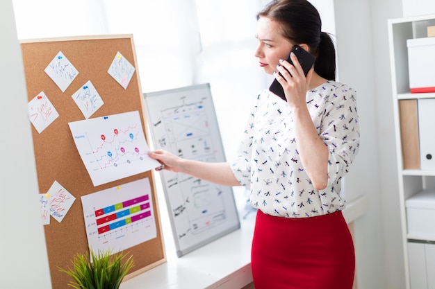 A young girl standing in the office near the Board with stickers and talking on the phone.