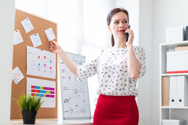 A young girl standing in the office near the Board with stickers and talking on the phone.