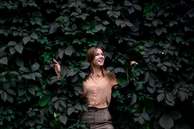 Young girl stands in green leaves alone with nature, a woman touches plants and dreams, a concept of a man in nature