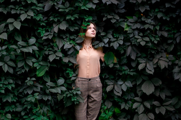 Young girl stands in green leaves