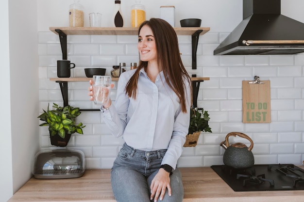 a young girl stands in the kitchen holding a glass of clean water