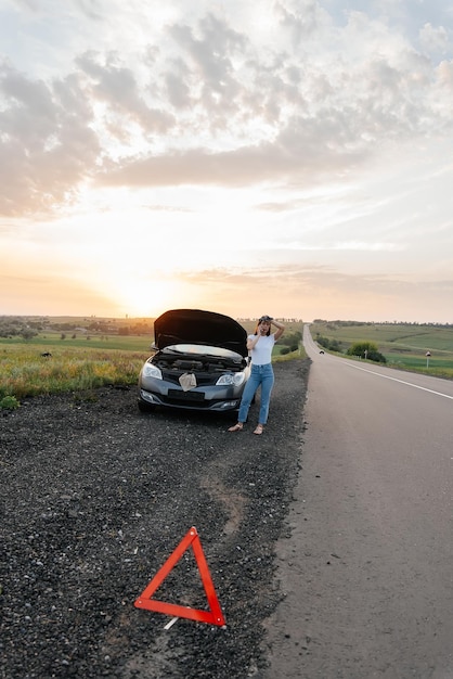 A young girl stands near a brokendown car in the middle of the
highway during sunset and tries to call for help on the phone
waiting for help car service car breakdown on road