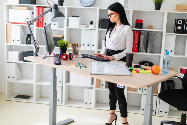 A young girl stands near a table and prints on the keyboard