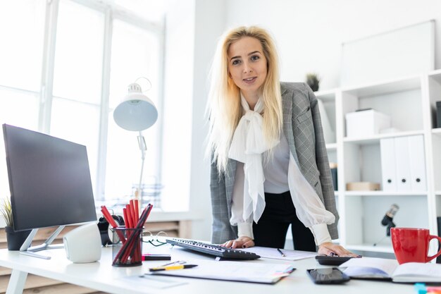 A young girl stands in the office, hands on the table.