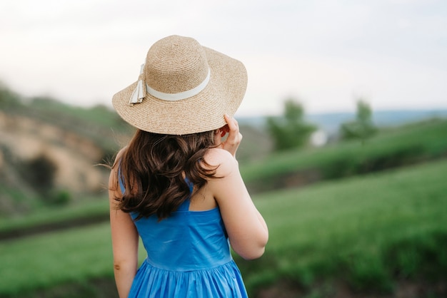 Молодая девушка в соломенной шляпе с большими полями на горных зеленых склонах