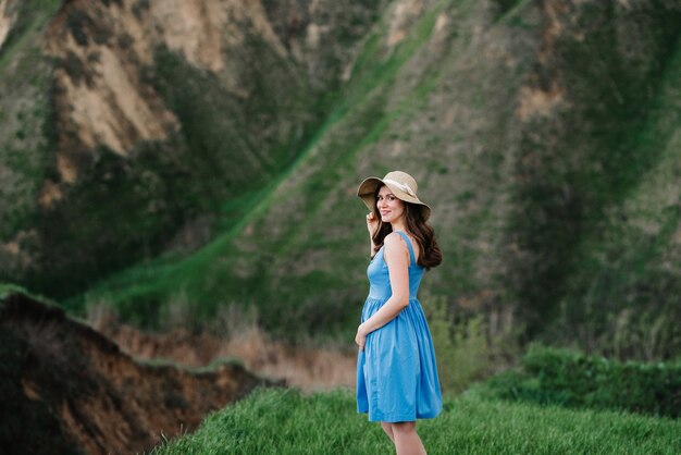 Молодая девушка в соломенной шляпе с большими полями на горных зеленых склонах