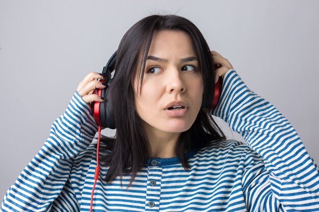 A young girl in a striped vest is listening to music in red headphones in a studio and dancing.