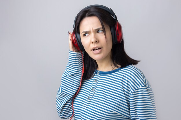 A young girl in a striped vest is listening to music in red headphones in a studio and dancing.