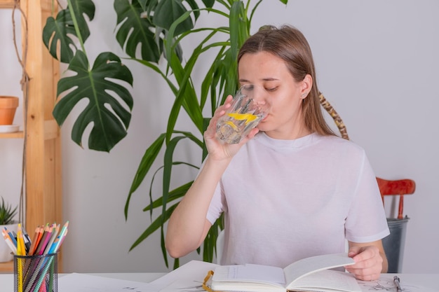 A young girl student drinks water during the learning process Pure water with lemon Student drinks water at home doing homework