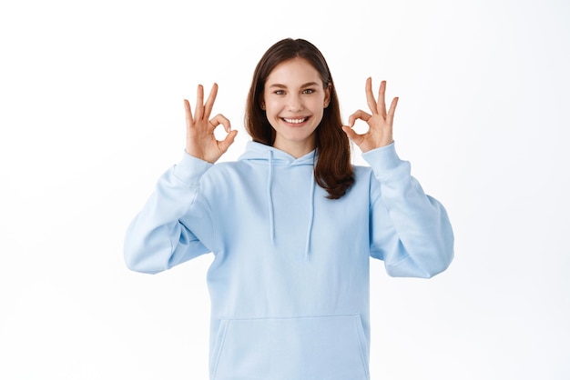 Young girl student say yes showing okay signs in approval accept something good praise choice Woman show OK gesture as like and compliment thing standing over white background