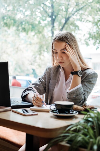 ノートパソコンのスマートフォンとオンラインで学ぶコーヒーの学生と一緒にカフェに座っている若い女の子の学生