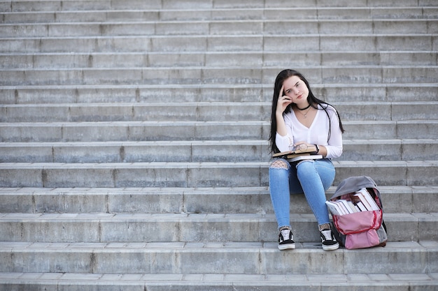 バックパックと本を持って路上で若い女の子の学生