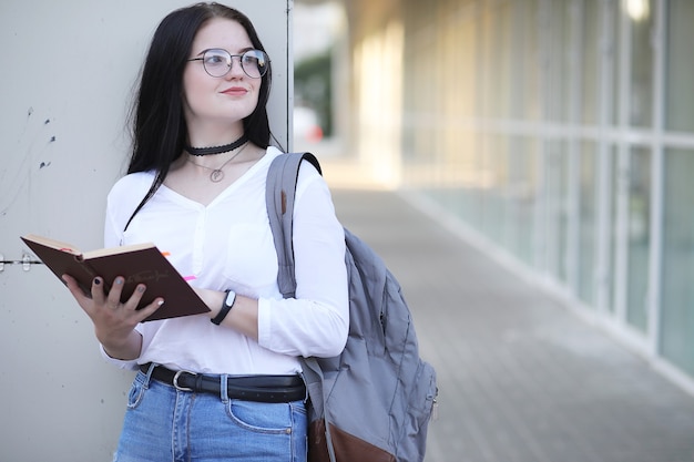 バックパックと本を持って路上で若い女の子の学生