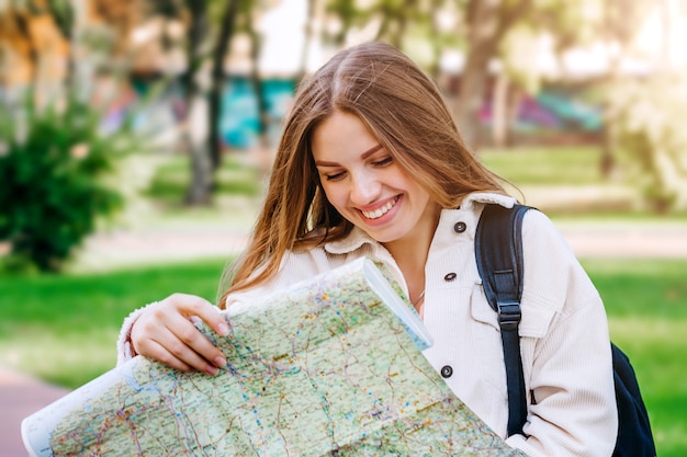 A young girl student walks around the city with a map and looking for a way. 