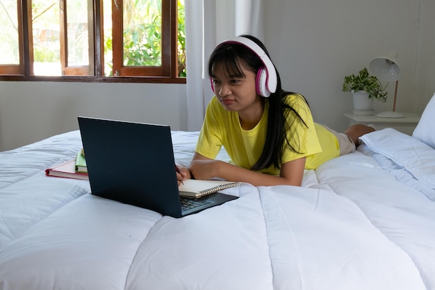 Young girl studying with laptop on bed in bedroom