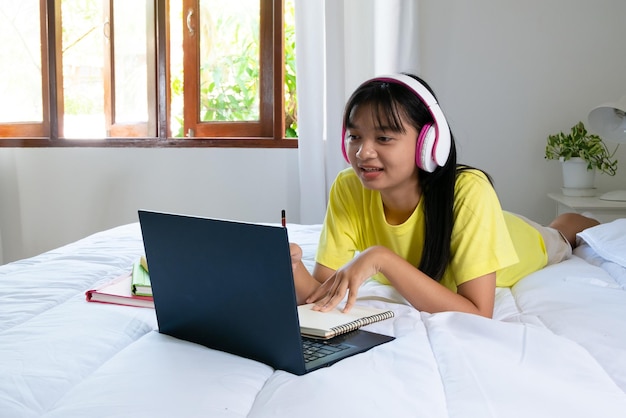 Photo young girl studying with laptop on bed in bedroom