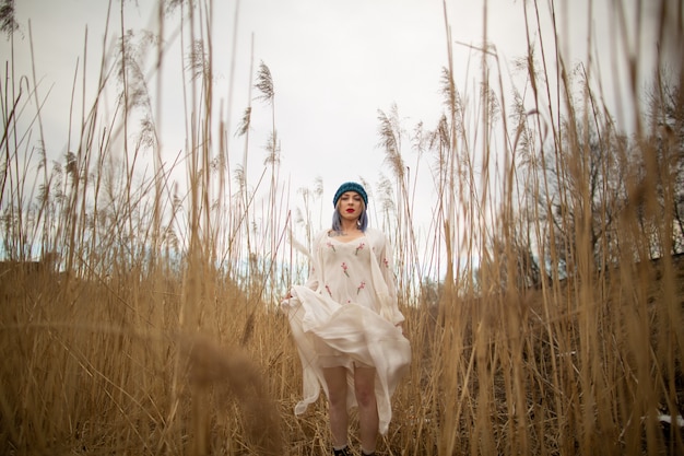 Una giovane ragazza in un cappello elegante e abito bianco a piedi in un campo di grano